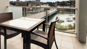 Un balcón con mobiliario de mimbre que ofrece vistas a un paisaje urbano, un río y barcos.