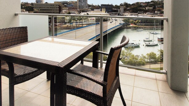 Un balcón con mobiliario de mimbre que ofrece vistas a un paisaje urbano, un río y barcos.