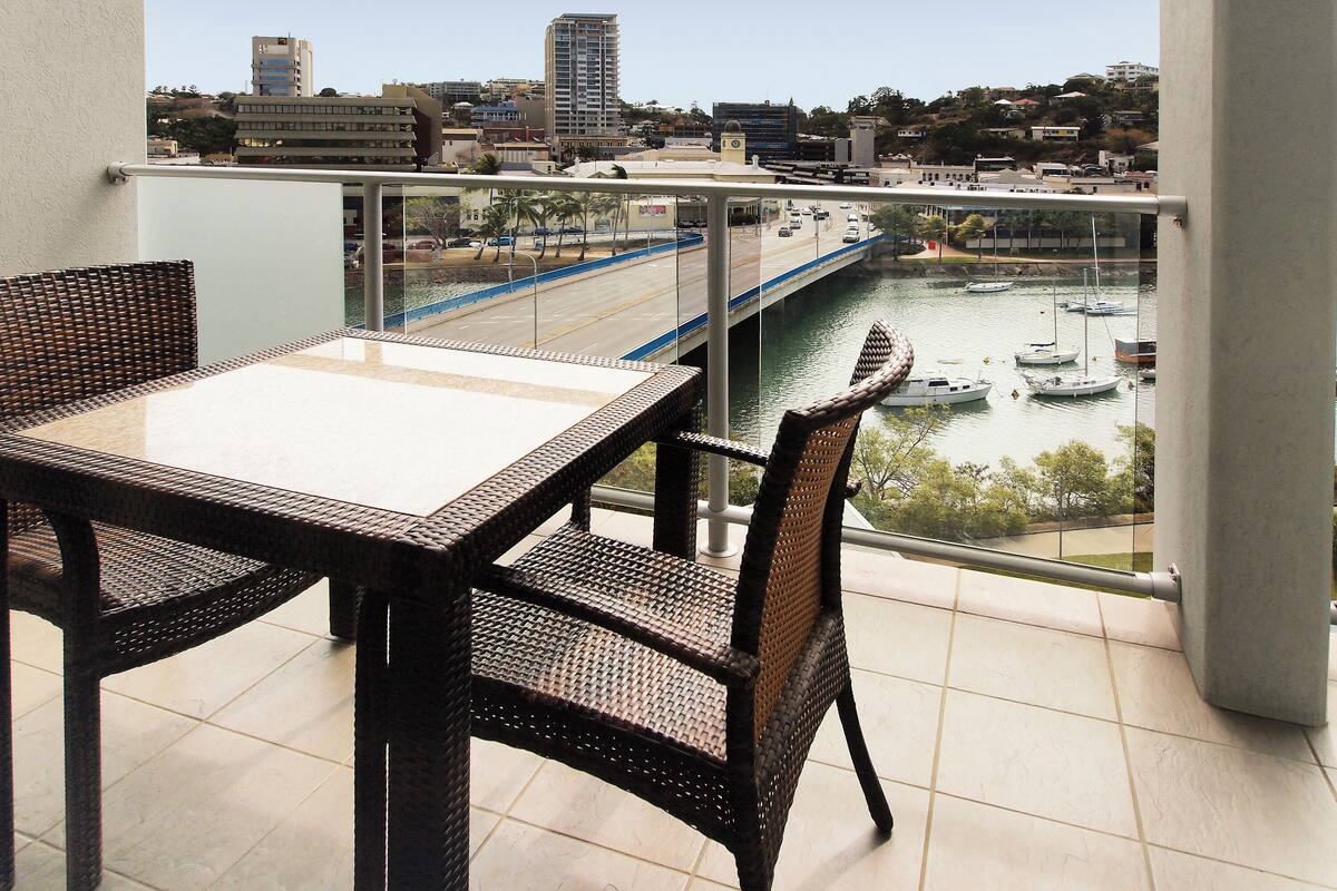 A balcony with wicker furniture overlooking a cityscape, a river, and boats.