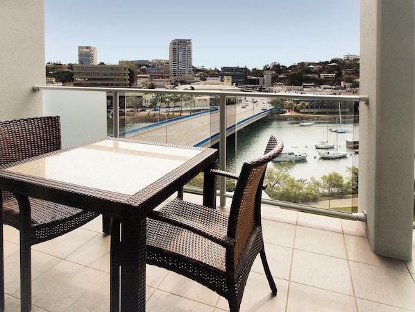 Ein Balkon mit Korbmöbeln und Blick auf Stadtlandschaft, Fluss und Boote.