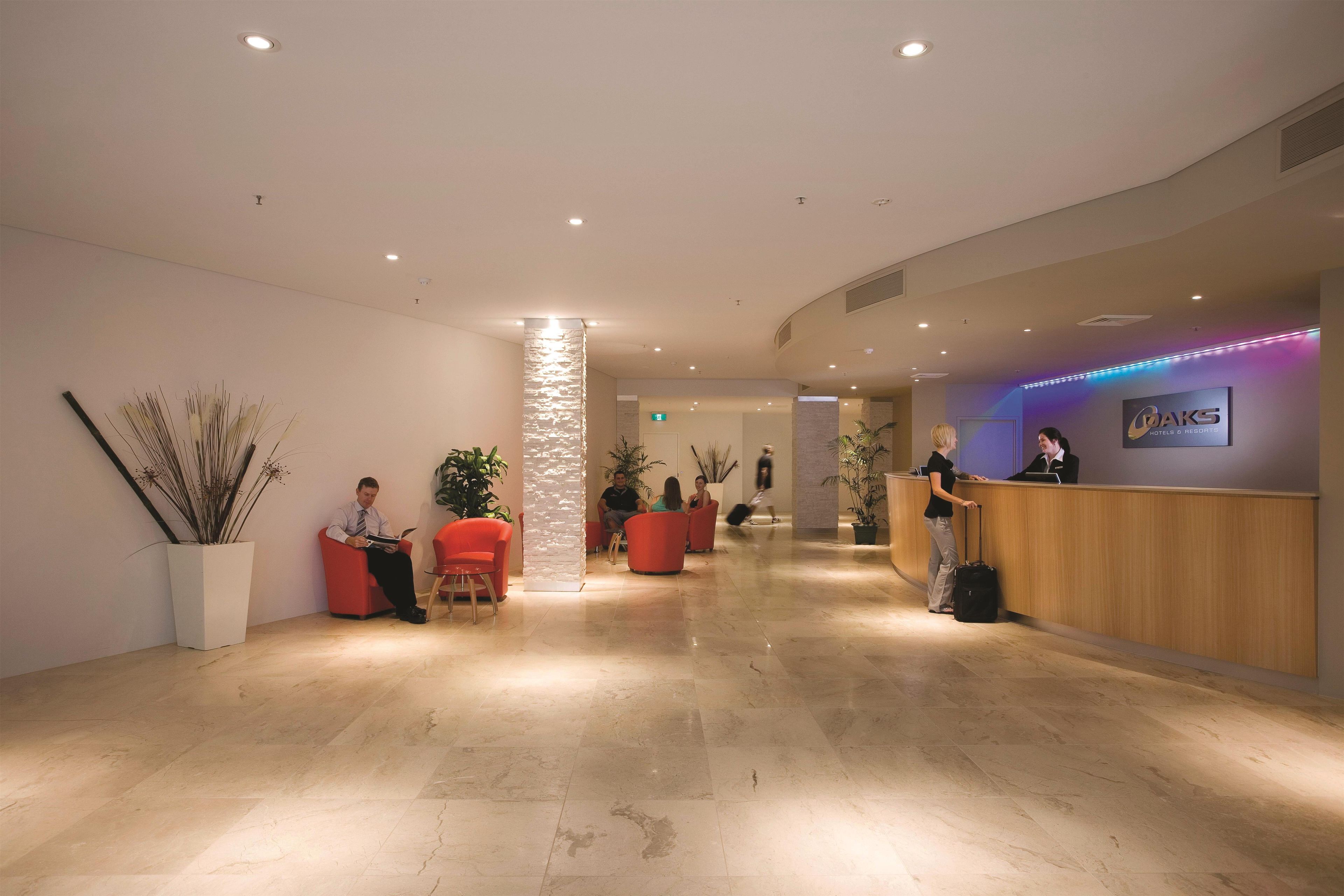 A hotel reception area with a wooden reception desk, red seating, and a column with a textured pattern.