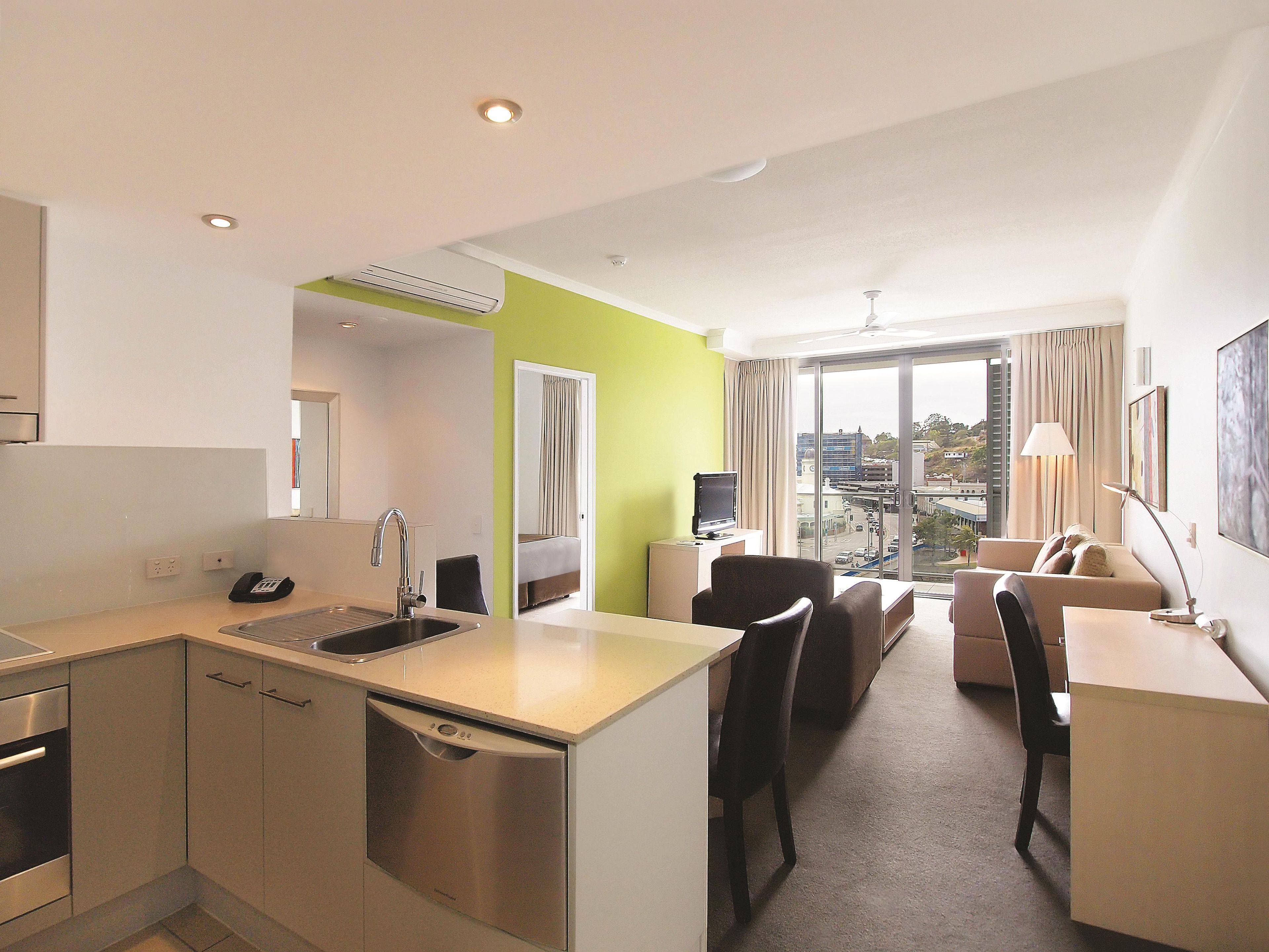 Habitación de hotel con kitchenette, comedor, sofá y un amplio ventanal con vistas a la ciudad.
