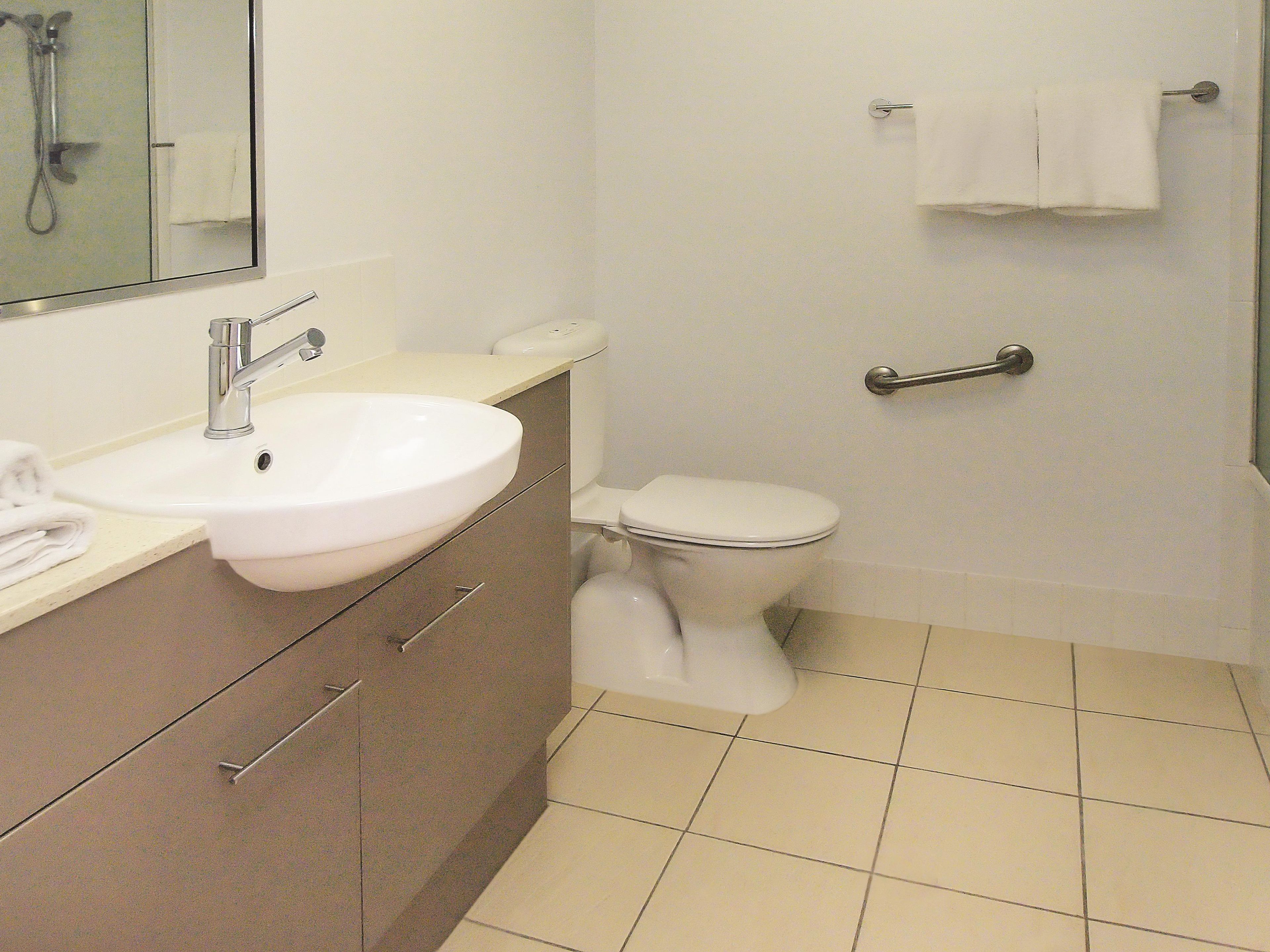 A bathroom with a sink, mirror, toilet, and a shower area.