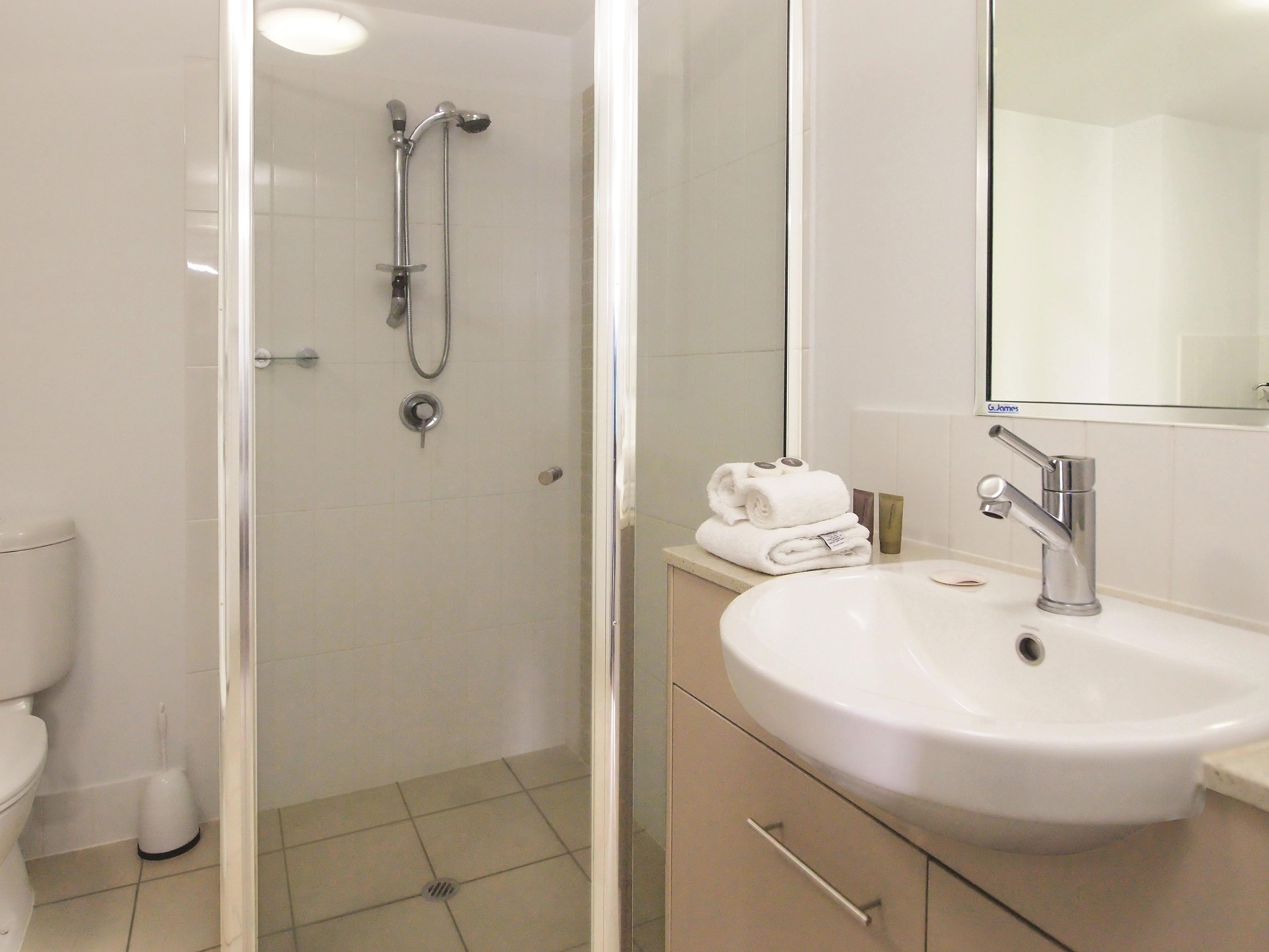 Een moderne badkamer met een douchecabine van glas, een witte wastafel en een spiegel erboven.