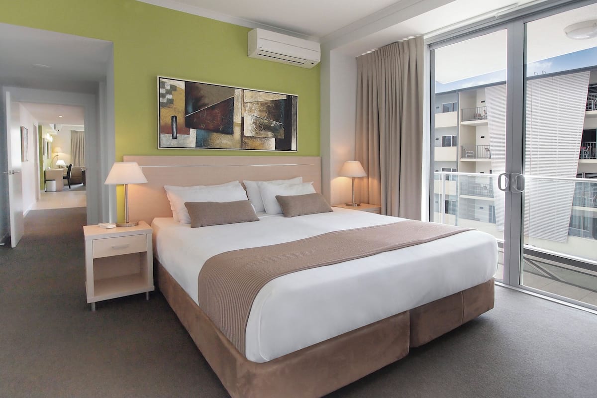 A hotel room with a large bed, two bedside tables with lamps, a green accent wall, and a view of the outside balcony.