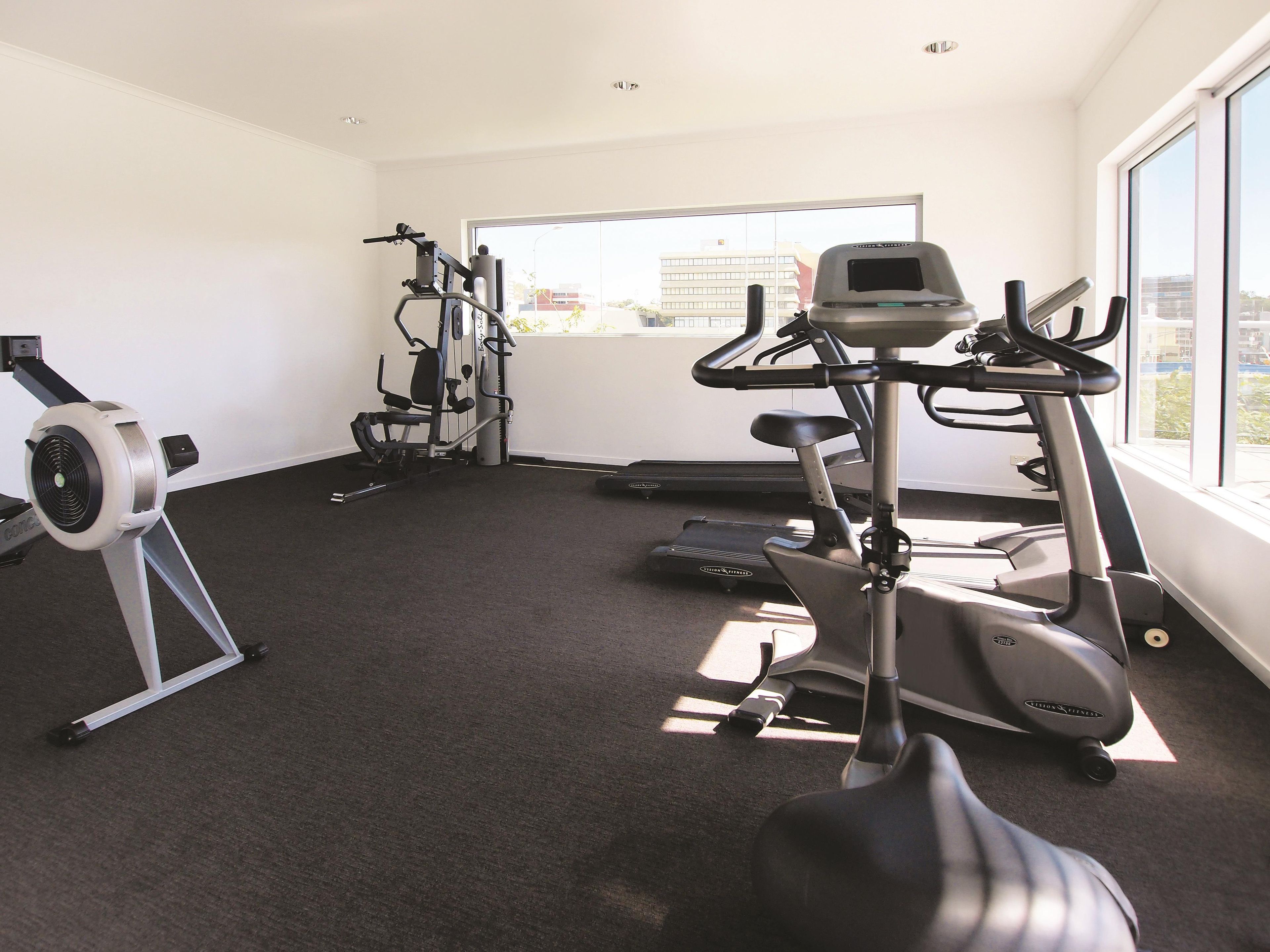 A gym with cardio machines, weight equipment, and a large window providing natural light.