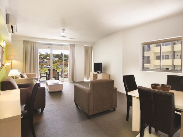 A hotel room with a balcony, a television, a dining area, and a sofa.