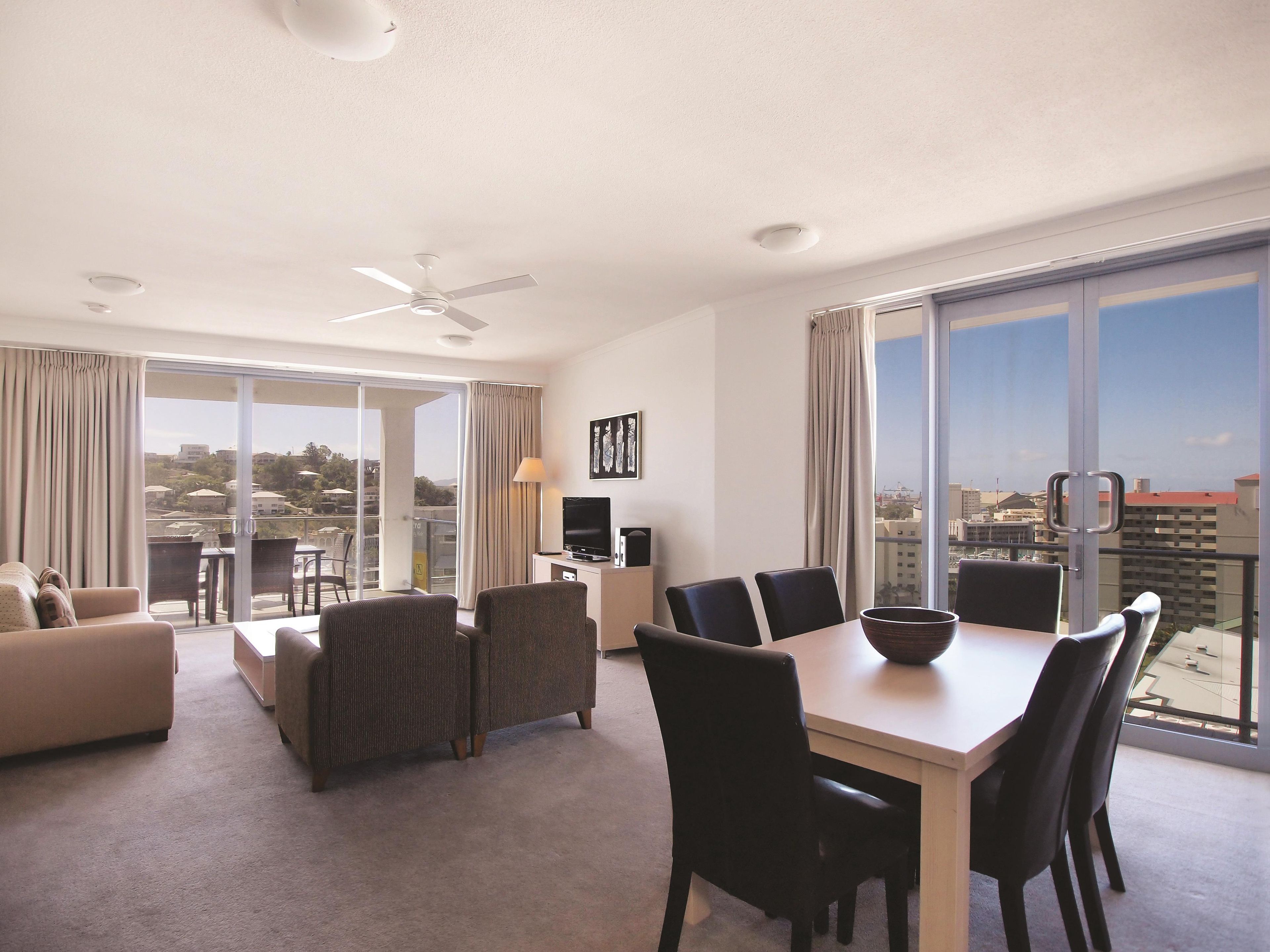 A hotel room with a balcony, a dining area, a sofa, and a television.