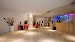 Un vestíbulo de hotel moderno con una recepción, zonas de estar y un pilar decorativo.