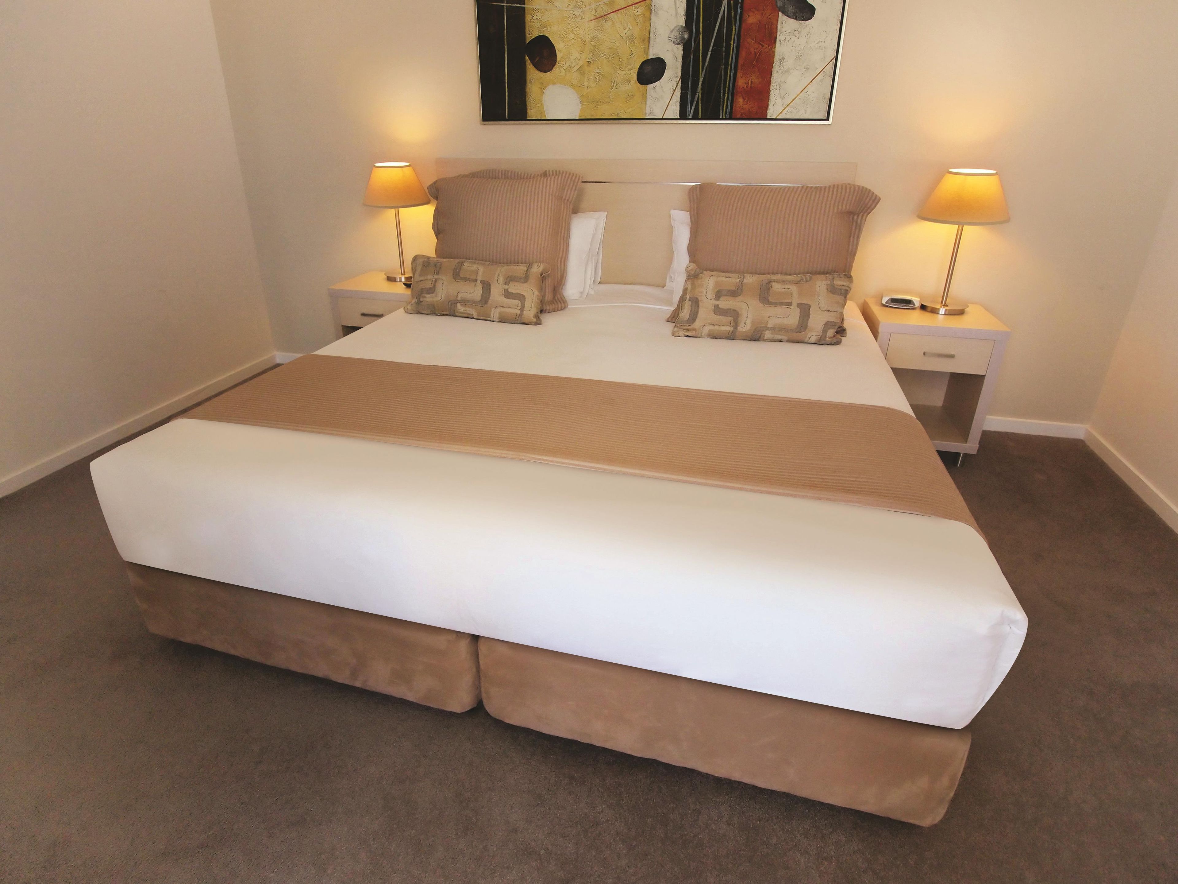 A neatly made bed with a white and brown bedspread, two pillows, and two bedside lamps.