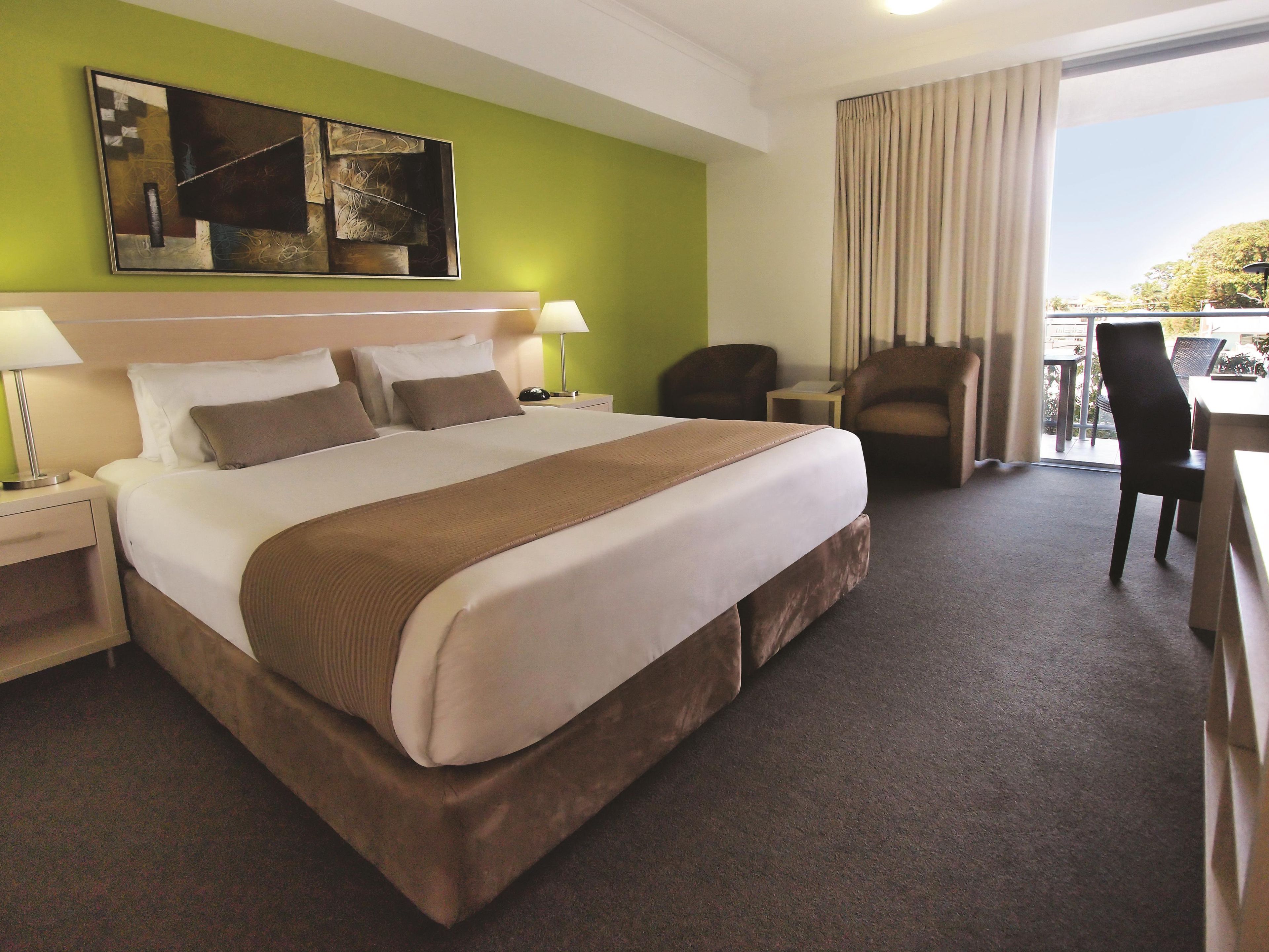 A hotel room with a large bed, a desk, a chair, and a view of the outdoors.