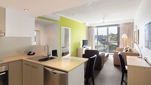 Habitación de hotel moderna con kitchenette, comedor y sala de estar con un amplio ventanal que ofrece vistas a la ciudad.