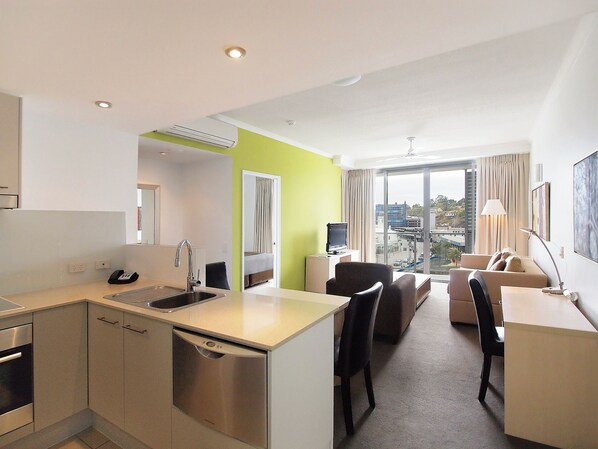 Ein modernes Hotelzimmer mit Küchenzeile, Essbereich und Wohnbereich mit großem Fenster und Blick auf die Stadt.