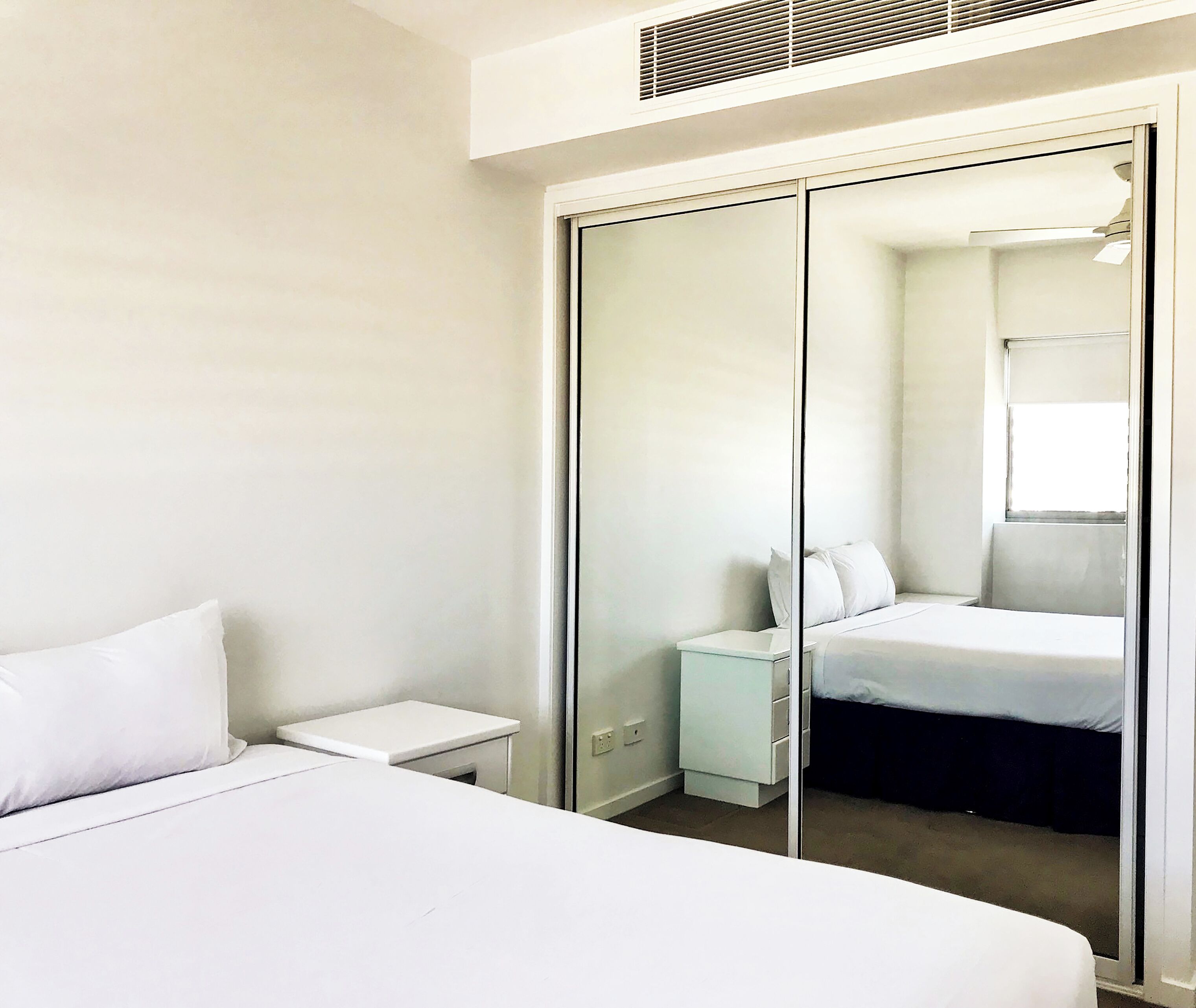 Una habitación de hotel con cama, mesita de noche, armario y espejo.