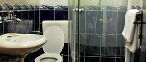 Un baño con inodoro blanco, lavamanos y cabina de ducha con mampara de vidrio.