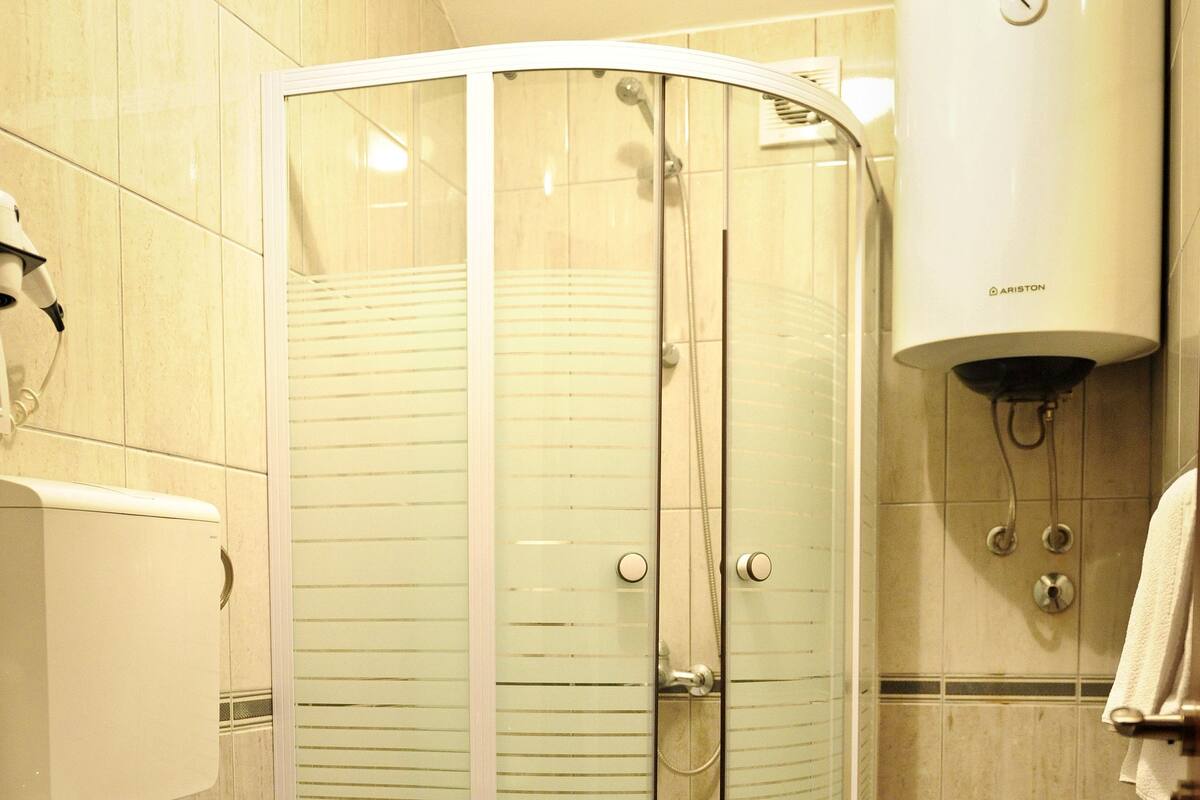A bathroom with a glass-enclosed shower, a toilet, and a wall-mounted heater.