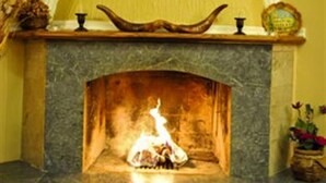 Una chimenea con un fuste de piedra, un estante decorativo arriba y una pequeña mesa a la derecha.