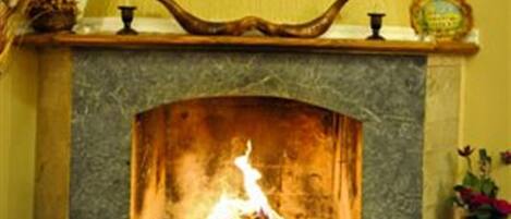 Una chimenea con un fuste de piedra, un estante decorativo arriba y una pequeña mesa a la derecha.