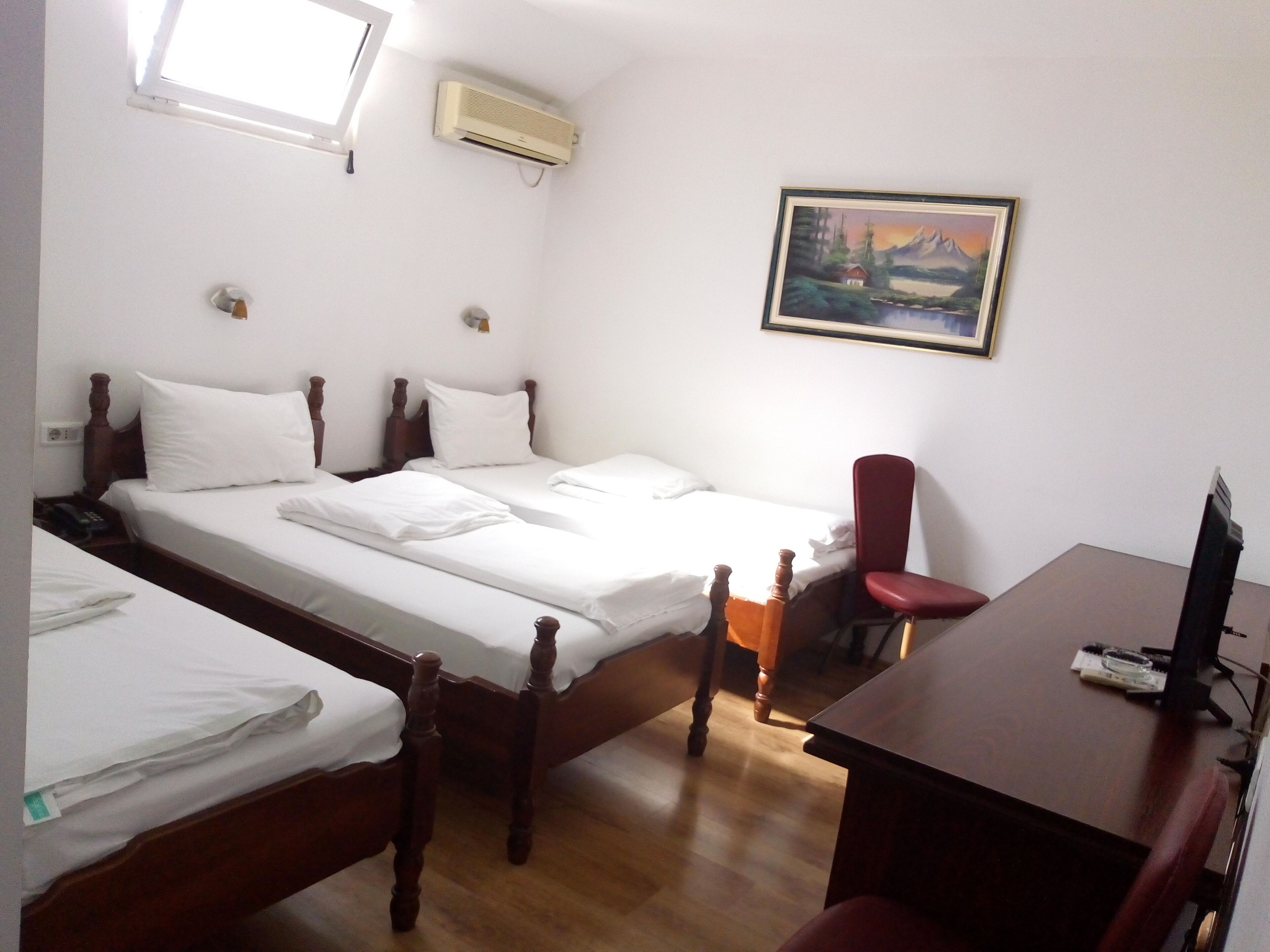 A hotel room with two wooden beds, a desk with a computer, a chair, and a painting on the wall.