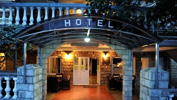Fachada de hotel de piedra, un letrero sobre la entrada y puerta de cristal que da al interior.