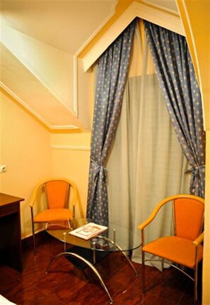 A corner room with a small table, two chairs, a window with patterned curtains, and a wooden floor. - Hotel Evropa (Podgorica)