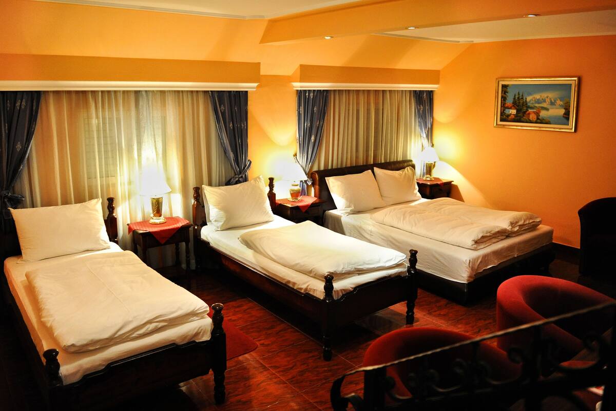 A hotel room with two single beds, a red armchair, and a painting on the wall.