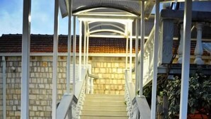 Una escalera con barandales blancos que conduce a una zona cubierta, flanqueada por muros de piedra y techo de ladrillo.