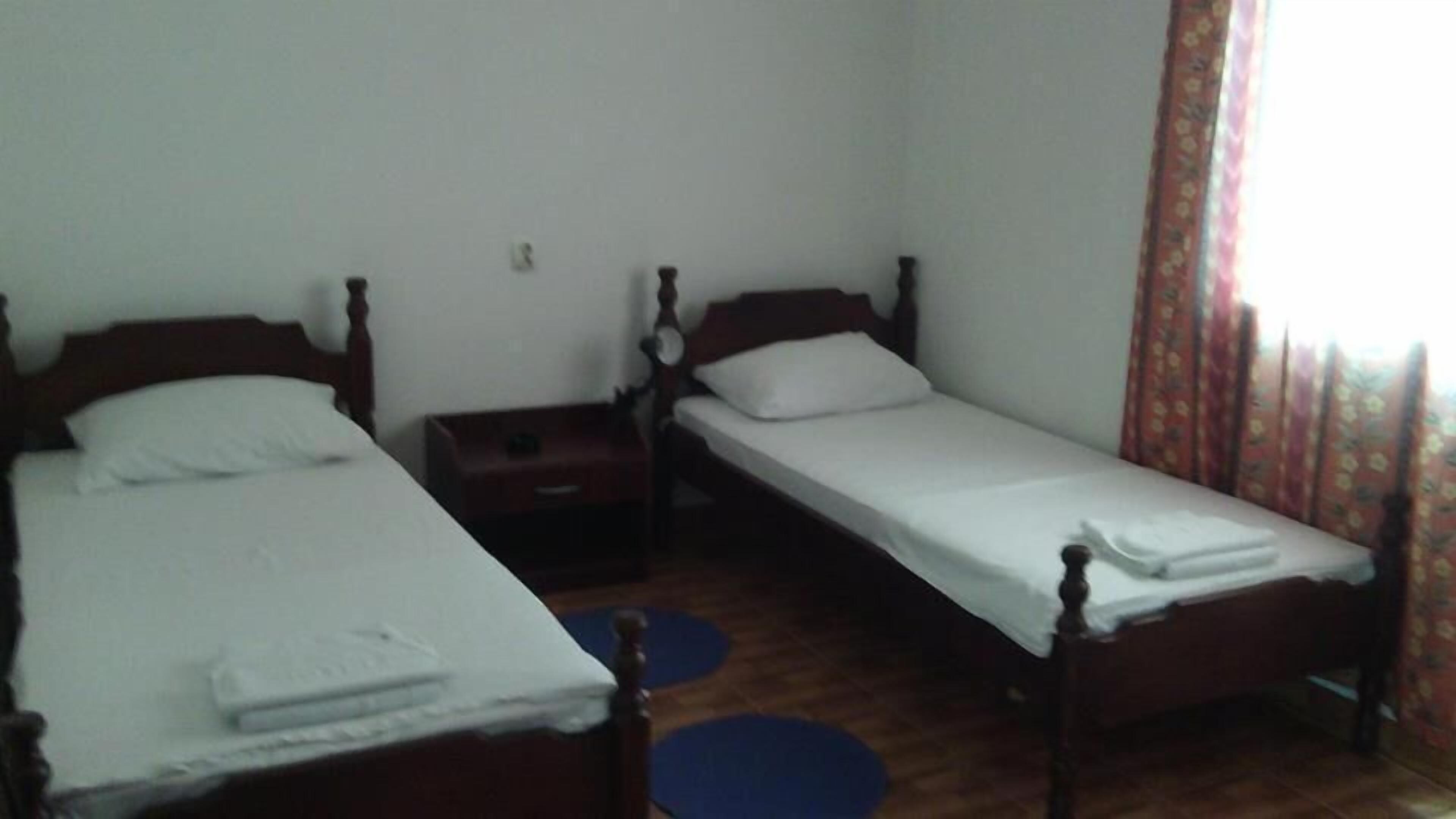 Una habitación con dos camas individuales, una mesita pequeña y un tapete azul en el suelo.