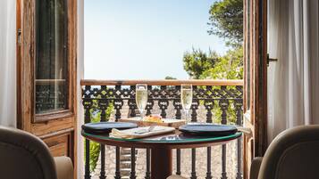Un balcón con una mesa dispuesta para dos personas, que incluye una copa de vino blanco, un plato de comida y una servilleta.
