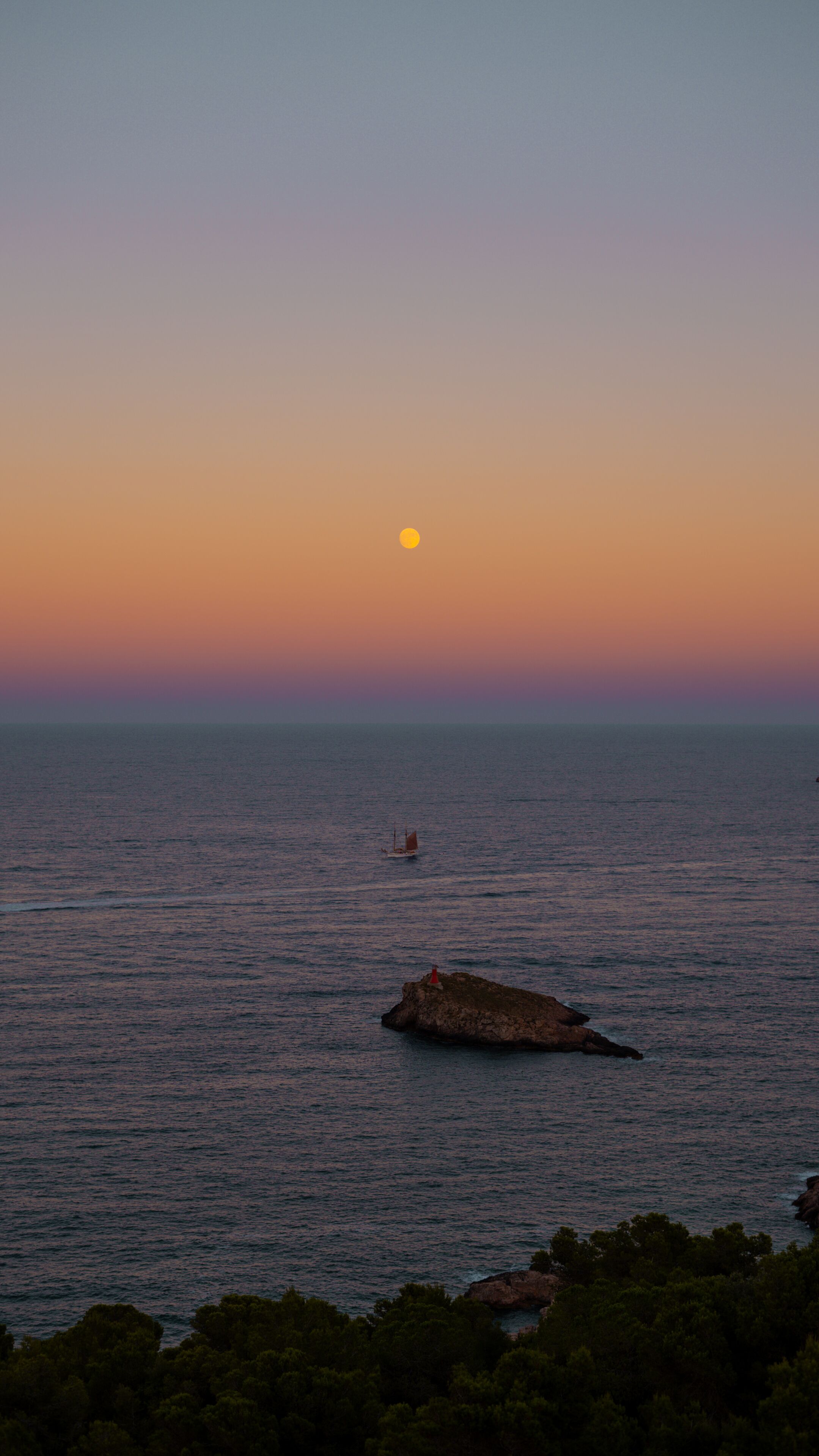A sunset over a calm sea with a small island and a boat.