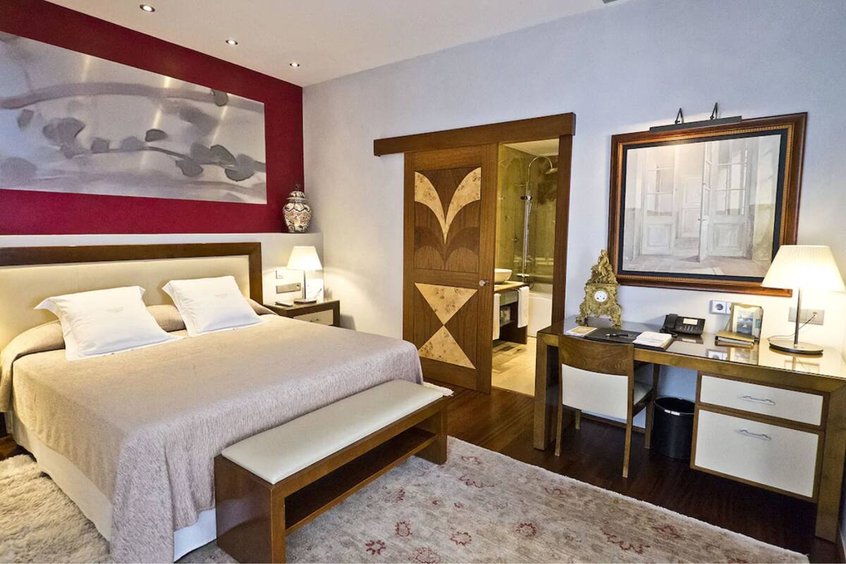 A hotel room with a bed, bedside tables, a desk, and a mirror.