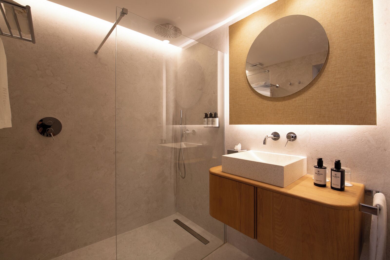 A modern bathroom with a glass-enclosed shower, a wooden vanity with a large mirror, and a beige tiled wall.