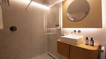 A modern bathroom with a glass-enclosed shower, a wooden vanity with a large mirror, and a beige tiled wall.