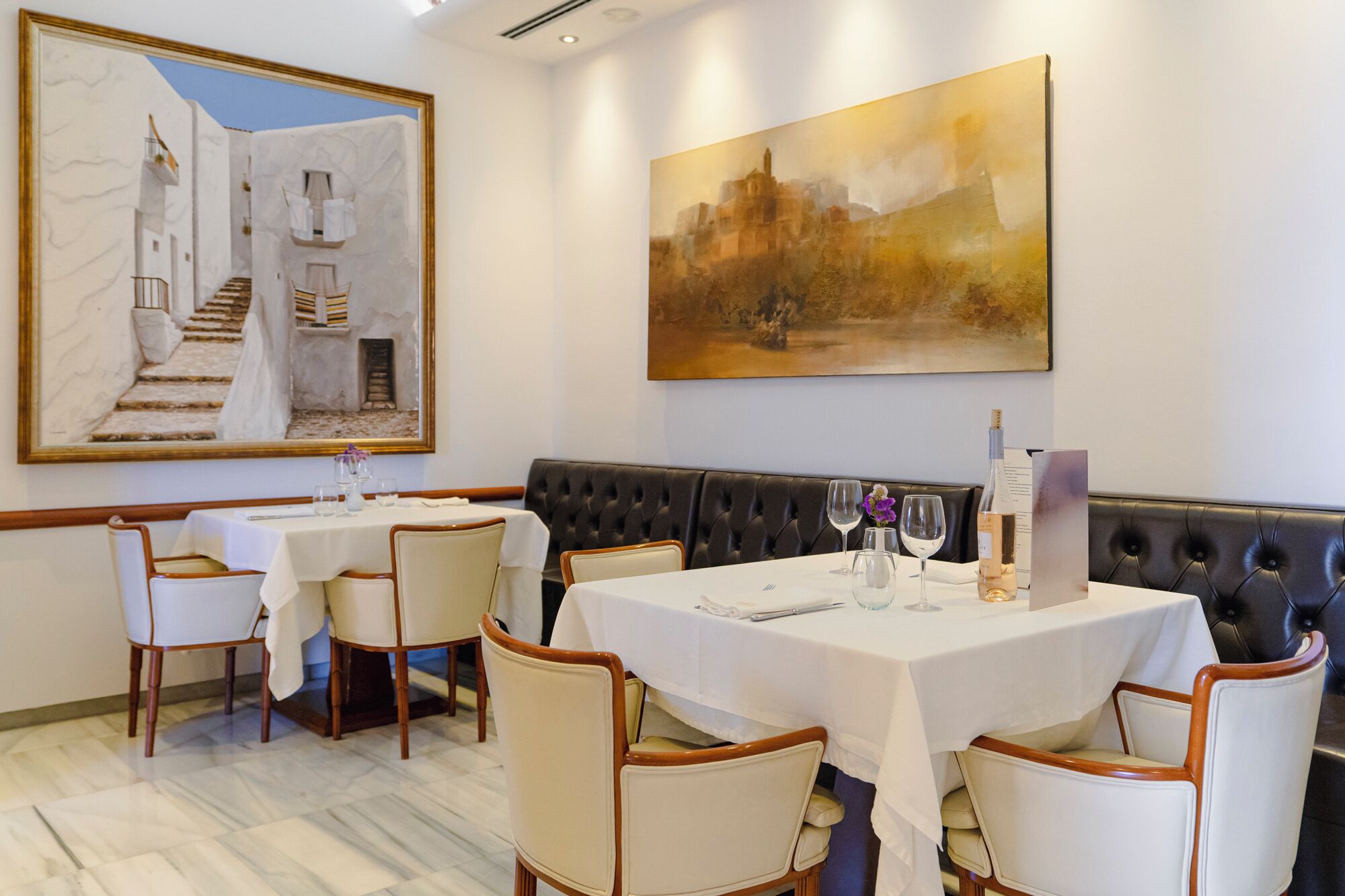 A restaurant with white tablecloths, leather booths, and a marble floor.