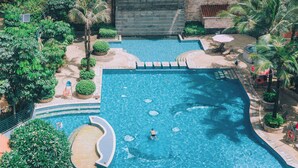 Una piscina al aire libre rodeada de exuberante vegetación, con un muro de piedra y palmeras.