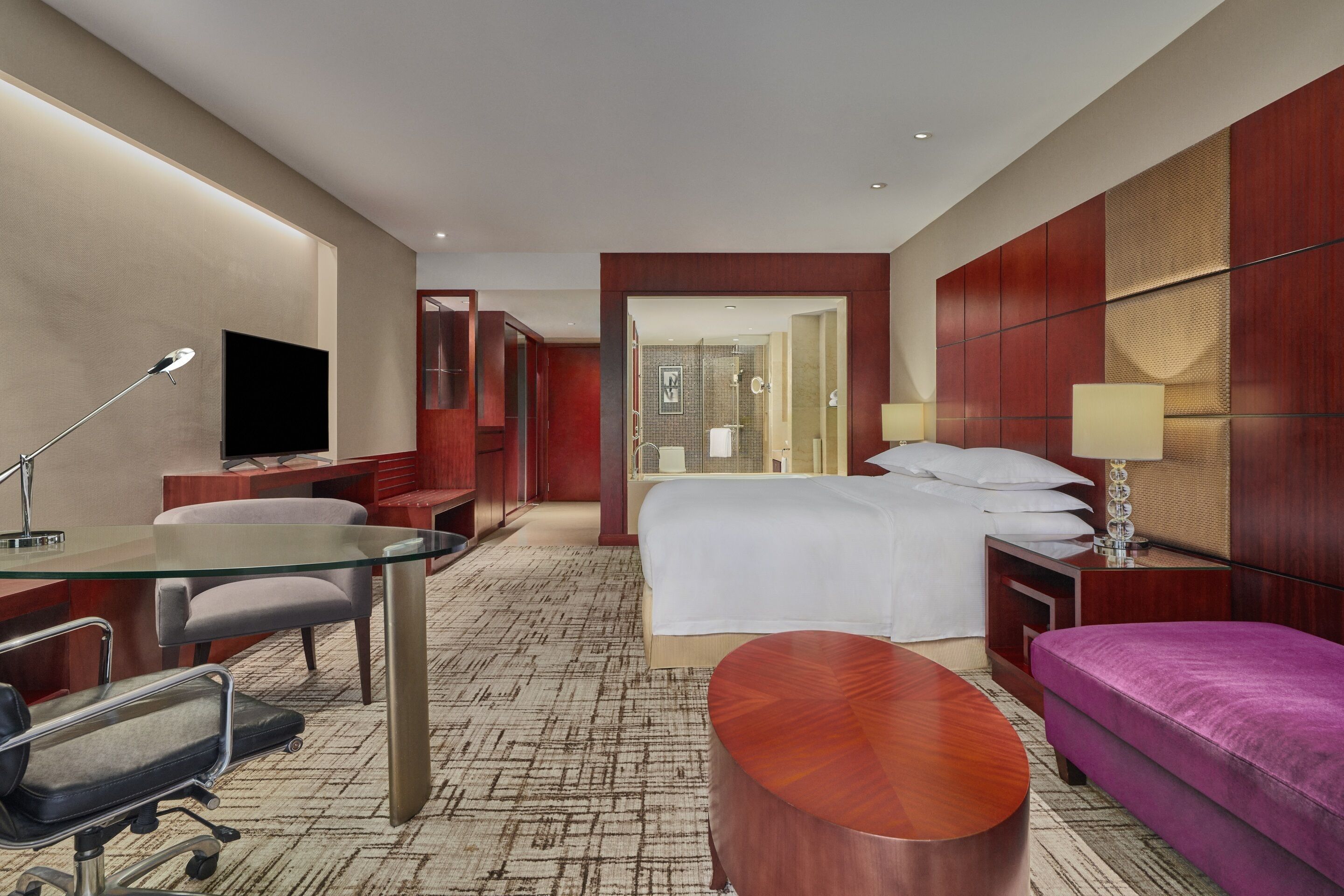 Une chambre d’hôtel comprenant un lit, un bureau avec une chaise, un canapé, une télévision et une salle de bain visible à travers une porte ouverte.