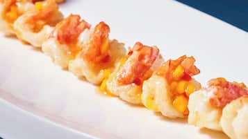 A white rectangular plate with a row of shrimp and corn on a bed of what appears to be rice or a similar grain, garnished with a small sprig of parsley.