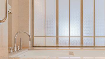 A bathroom with a bathtub, a faucet, and a window with frosted glass panels.