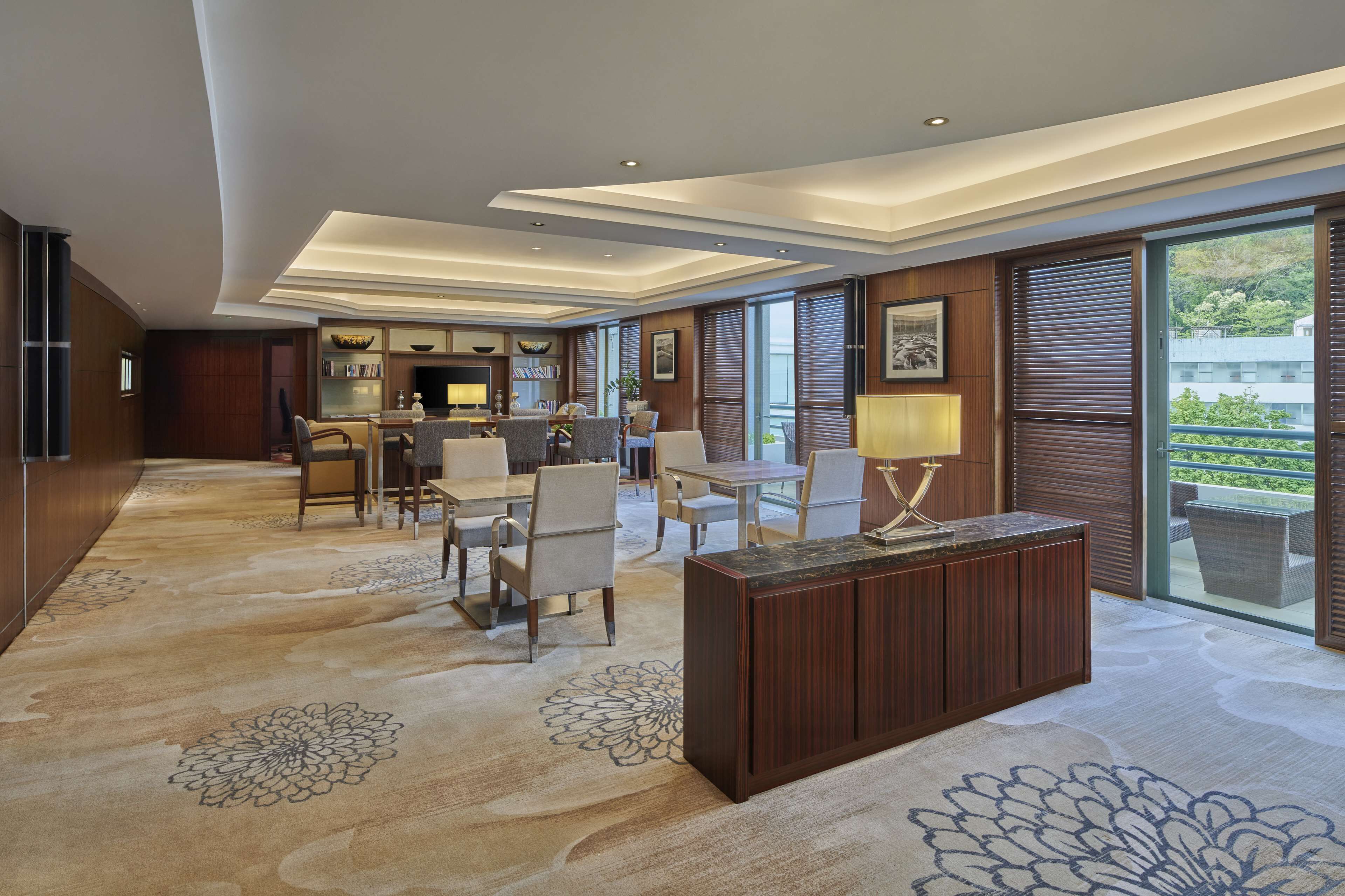 Een moderne hotellobby met een centraal zitgedeelte, een receptiebalie en grote ramen met uitzicht op het omliggende landschap.