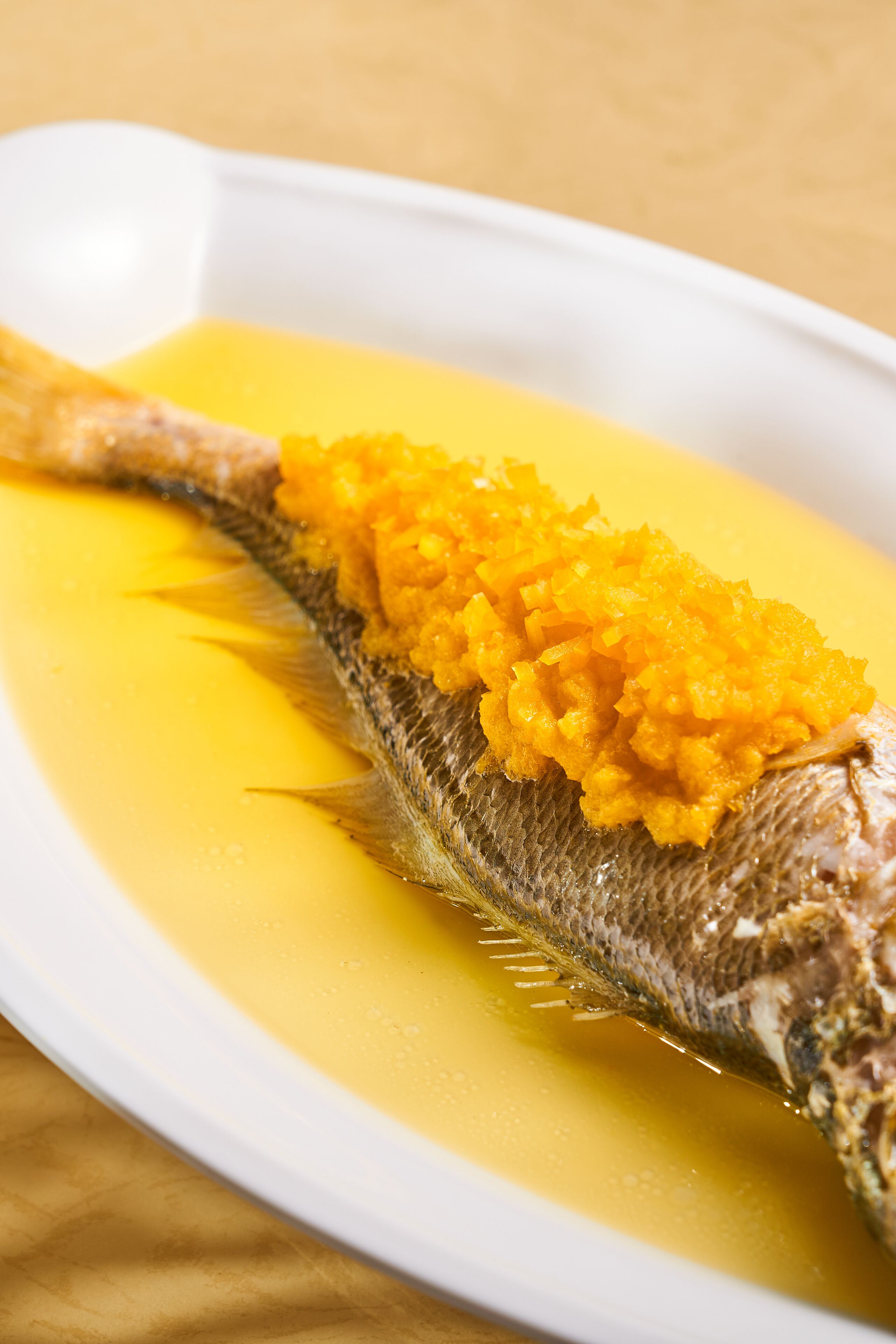 A white plate with a whole fish topped with a yellow sauce and a side of mashed yellow vegetables.