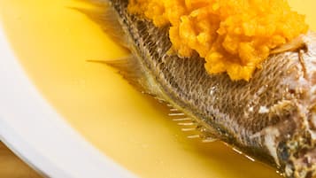 A white plate with a whole fish topped with a yellow sauce and a side of mashed yellow vegetables.