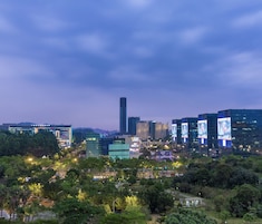 A cityscape at dusk with modern buildings, a prominent skyscraper, and illuminated signage.