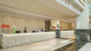 A hotel reception area with a modern design, featuring a reception desk, seating area, and a large, open space with a high ceiling and skylights.