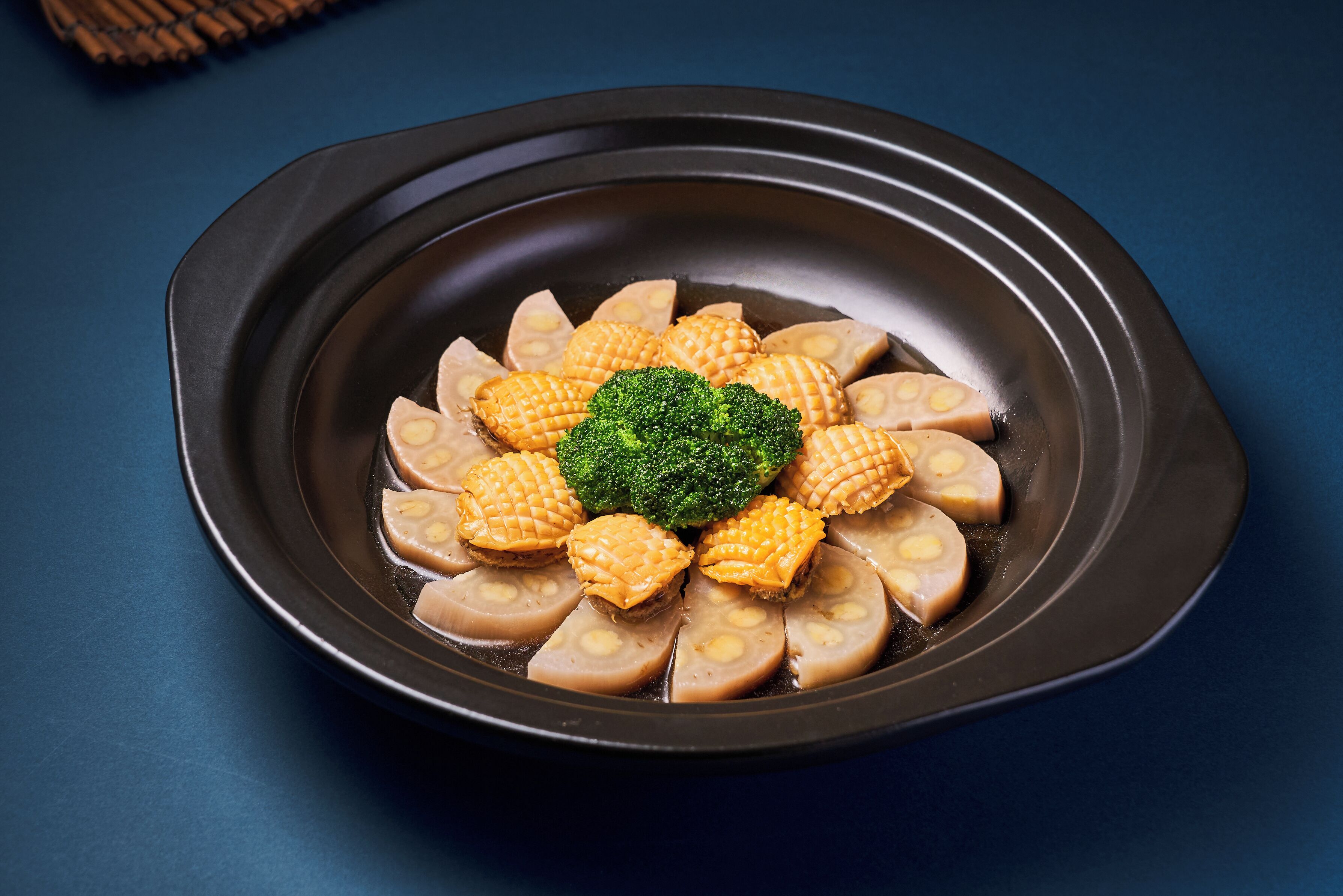 A plate with sliced tofu and a broccoli center on a dark plate.