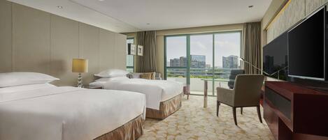 A hotel room with two beds, a desk, a chair, a TV, and a large window offering a city view.