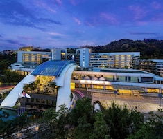 A modern hotel with a curved glass facade, multiple floors, and a parking area.