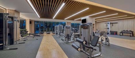 Een moderne sportschool met diverse fitnessapparaten, grote ramen en een houten vloer.