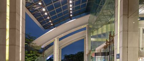 A modern hotel entrance with a glass facade, a spacious lobby, and a prominent atrium with natural light.