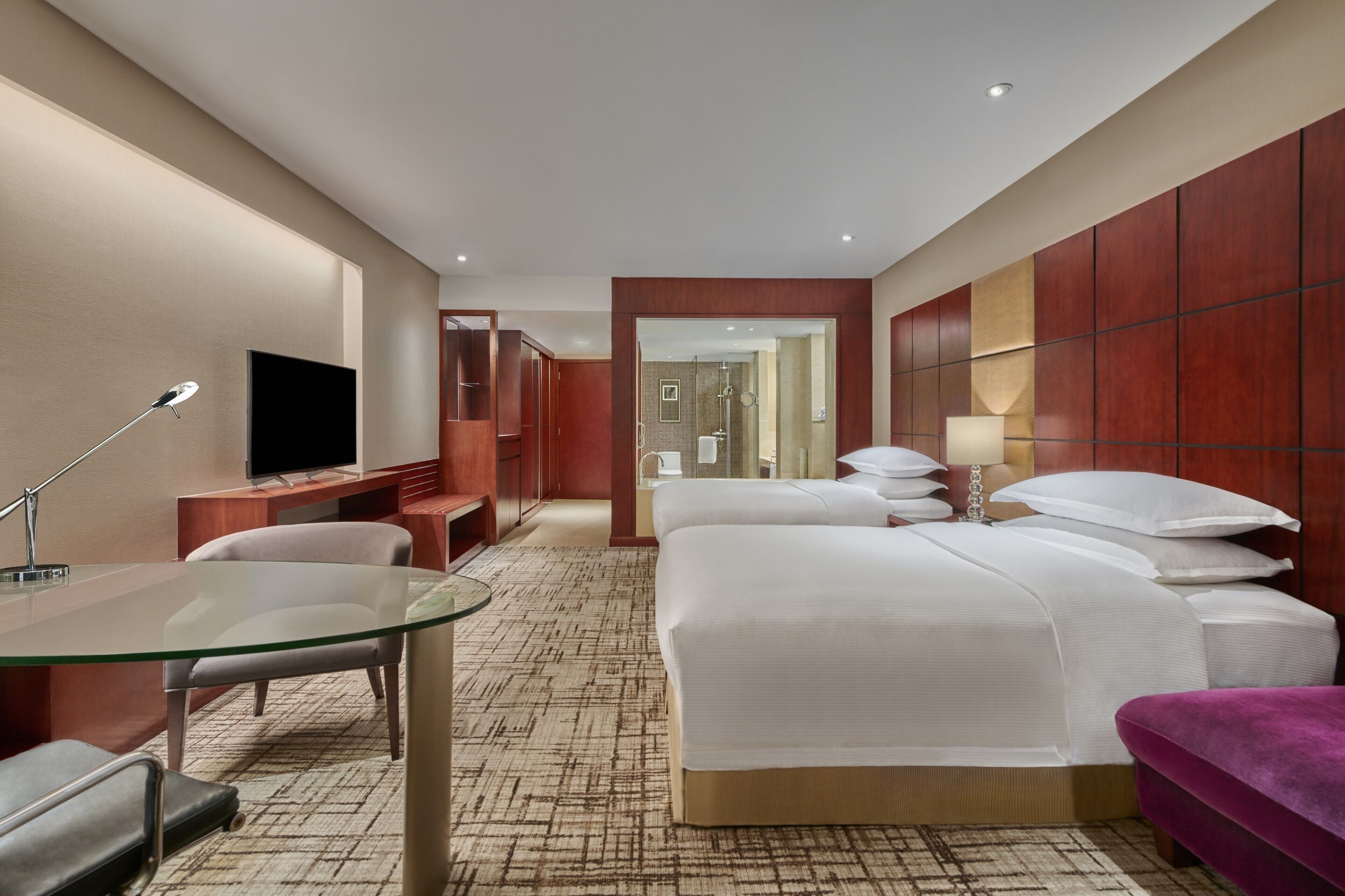 A hotel room with a bed, a desk with a chair, a television, and a glass table.