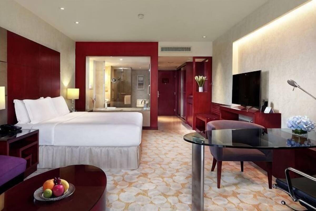 Une chambre d’hôtel avec un lit, un bureau, une télévision et une table à manger avec des fruits.